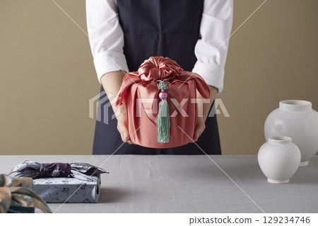 A woman wrapping a gift using bojagi (traditional Korean wrapping cloth). Reusable, handmade gift wrap for Korean holidays and anniversaries. A woman wrapping a gift using bojagi (traditional Korean wrapping cloth). Reusable, handmade gift wrap for Korean holidays and anniversaries. 129234746