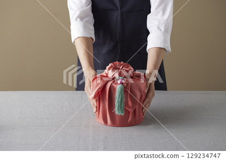 A woman wrapping a gift using bojagi (traditional Korean wrapping cloth). Reusable, handmade gift wrap for Korean holidays and anniversaries. A woman wrapping a gift using bojagi (traditional Korean wrapping cloth). Reusable, handmade gift wrap for Korean holidays and anniversaries. 129234747