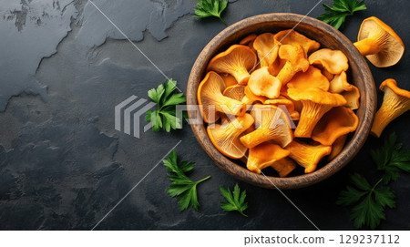 Fresh chanterelle mushrooms in wooden bowl with parsley leaves on dark stone background, rustic food concept. 129237112