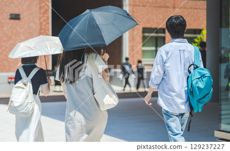 Back view of a group of male and female students walking with parasols 129237227