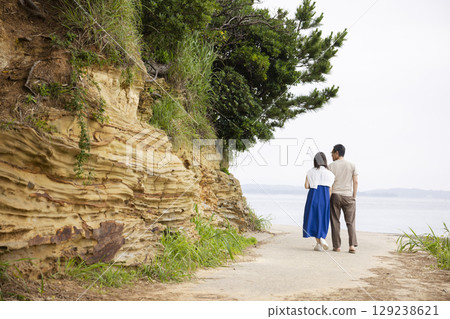 Back view of a couple walking along the coast 129238621