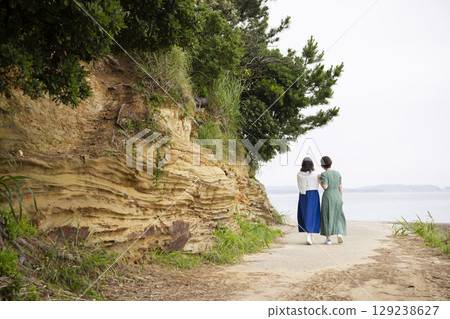 Back view of a woman walking along the coast 129238627