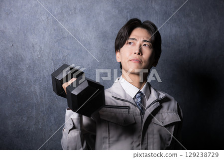 Image of a strong manufacturing worker in work clothes holding dumbbells, close-up 129238729