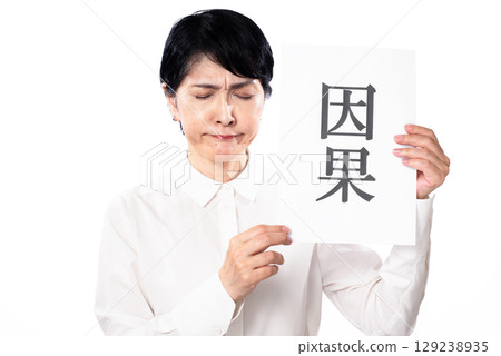 一位身穿白襯衫的中年婦女拿著一張寫著「原因」的紙，低頭看著 129238935