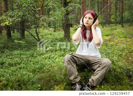 Young girl listening music with headphones in forest 129239457