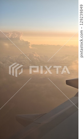 View from airplane window during golden sunset with fluffy clouds glowing in warm light View from airplane window during golden sunset with fluffy clouds glowing in warm light 129239849