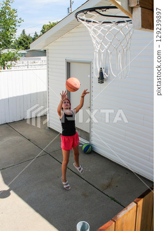 Teen Girl Shooting Basketball Into Hoop at Home 129239897