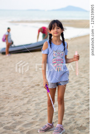 Young Girl with Bubble Wand on Serene Beach at Dusk 129239905
