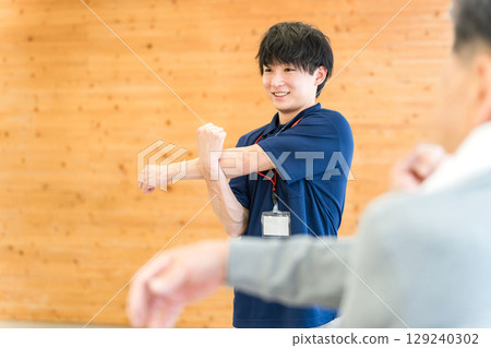 Male staff including sports trainer, caregiver and care manager doing stretching exercises at day care center for nursing care facility 129240302