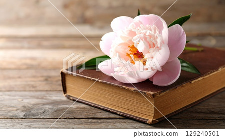 Pink peony blossom on a vintage book, a beautiful floral bouquet on a wooden background 129240501
