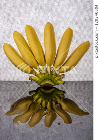 Yellow, ripe mini bananas with reflection on gray background Yellow, ripe mini bananas with reflection on gray background 129240604