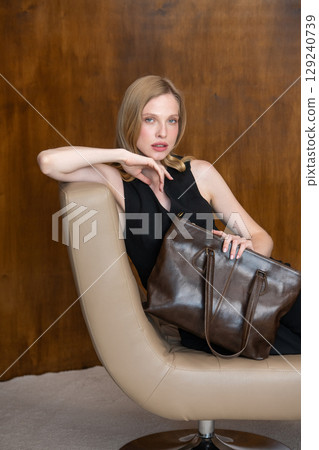 woman with wavy hair seated in a beige chair posing with a rich, 129240739