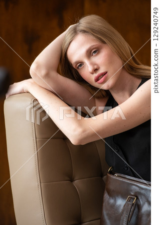 woman with wavy hair seated in a beige chair posing with a rich, 129240749