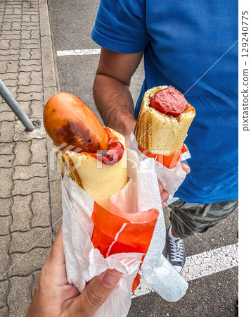 Street food hot dogs in baguette-style buns, held in hands. Outdoor casual meal. High quality photo 129240775