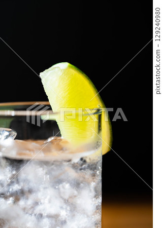 [雞尾酒配料] 在黑色背景下，將一杯美味的金湯力倒入加冰的玻璃杯中 [飲料配料] 129240980