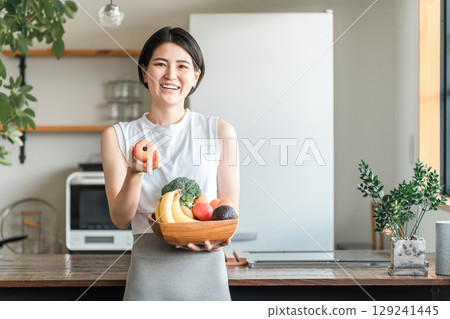 一位身穿運動服的年輕亞洲女性在廚房前拿著蔬菜(缺乏蔬菜、營養平衡、綠色和黃色蔬菜) 一位身穿運動服的年輕亞洲女性在廚房前拿著蔬菜(缺乏蔬菜、營養平衡、綠色和黃色蔬菜) 129241445