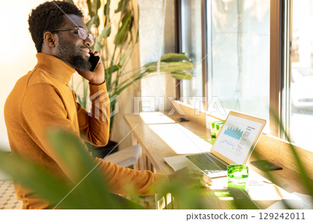 Businessman multitasking at modern workspace speaking on mobile phone and typing on laptop in office Businessman multitasking at modern workspace speaking on mobile phone and typing on laptop in office 129242011