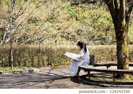 一位女士坐在環繞著一棵樹的長椅上看地圖 129242580