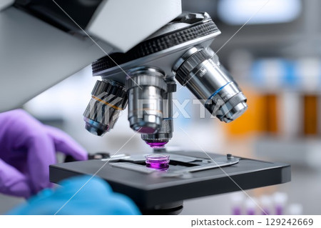 Microscope research work with scientist adjusting petri dish. Close-up of sample under lens in science lab. Blue gloves ensure hygienic conditions for experiment. Microscope research work with scientist adjusting petri dish. Close-up of sample under lens in science lab. Blue gloves ensure hygienic conditions for experiment. 129242669