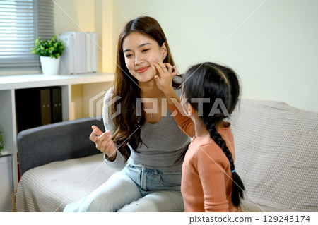 Cute little girl applying face cream on her mother cheek during a fun skincare routine Cute little girl applying face cream on her mother cheek during a fun skincare routine 129243174