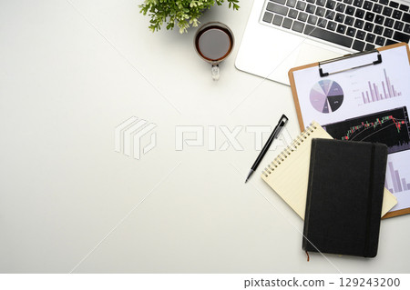 Flat lay of office desk with laptop, financial charts, notebooks, and coffee on white background 129243200