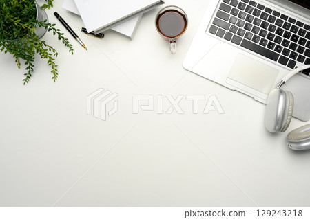 Minimalist workspace with laptop, coffee cup, headphones and notebooks on white desk 129243218