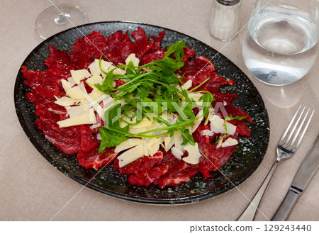 Raw veal meat carpaccio with cheese and fresh arugula 129243440