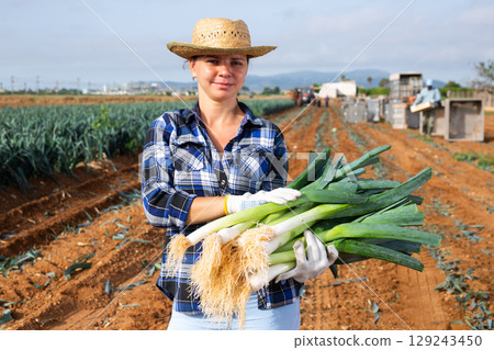 Successful female horticulturist with leeks in hands standing on field Successful female horticulturist with leeks in hands standing on field 129243450