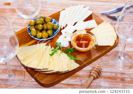 On wooden table there is cutting board with assorted cheese, honey, pickled olives - On wooden table there is cutting board with assorted cheese, honey, pickled olives - 129243533