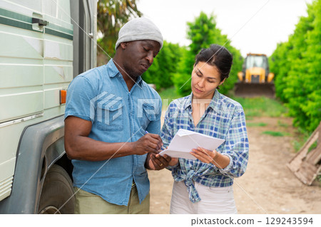 African farmer and asian woman discussing, standing at orchard 129243594