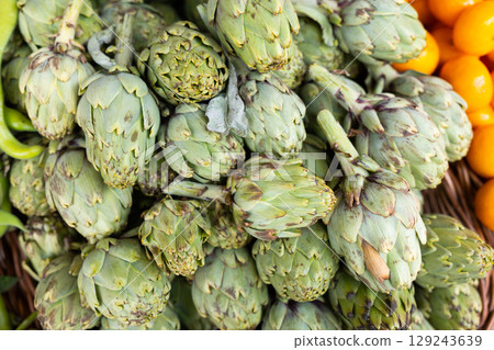 Pile of fresh artichoke globes on counter in store 129243639