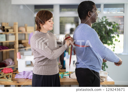 Seamstress measuring client in sewing studio for custom garment Seamstress measuring client in sewing studio for custom garment 129243671