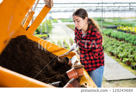 Hardworking young farmer woman fills a flower pot with nutritious soil 129243689