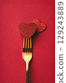 Valentine's day greeting card in minimal style with shiny heart pierced by golden fork on red background. 129243889