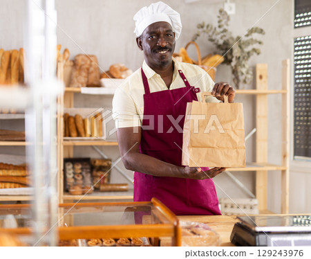 Male baker holding a brown paper bag in a bakery 129243976