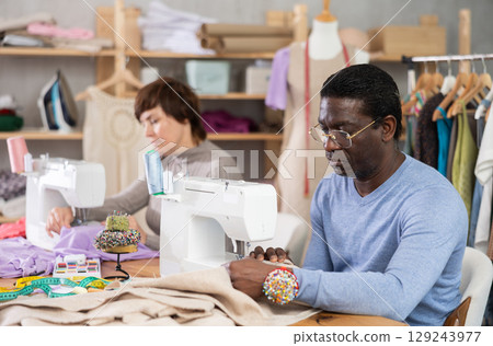 Woman tailor and African male companion sew clothes in sewing machine Woman tailor and African male companion sew clothes in sewing machine 129243977