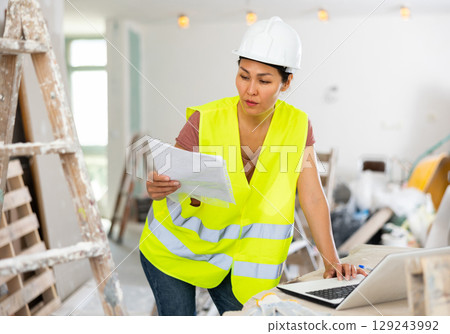 Woman engineer checking documents and using laptop during repair works 129243992