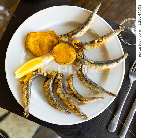 Fried anchovies with lemon on plate 129244002