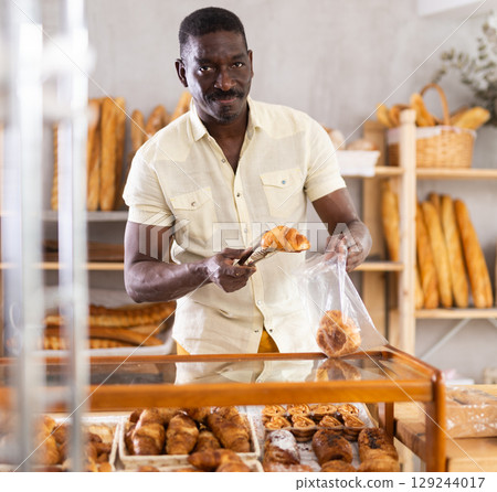 Male customer puts fresh croissants into bag at a bakery by himself. Self service concept 129244017