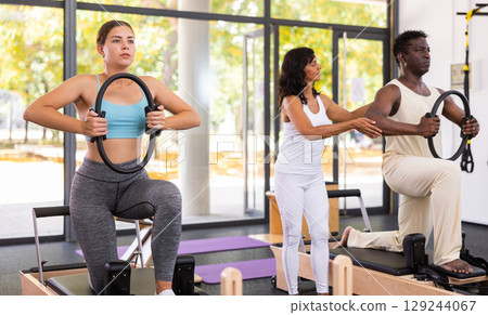 Latin female instructor helping African American man with ring in gym class 129244067