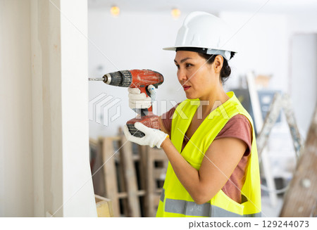 Asian woman repairer boring hole in wall with drill Asian woman repairer boring hole in wall with drill 129244073