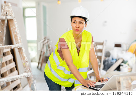 Woman builder using laptop in construction site Woman builder using laptop in construction site 129244115