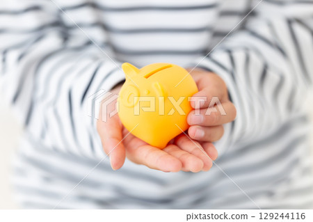 Elementary school boy holding a yellow piggy bank 129244116
