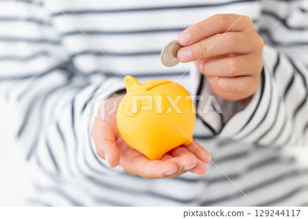 Elementary school boy putting money into a yellow piggy bank Elementary school boy putting money into a yellow piggy bank 129244117