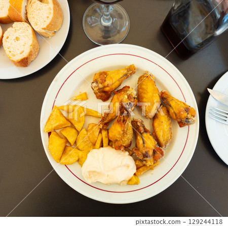 There is plate with fried chicken wings and portion of French fries and white sauce on table 129244118