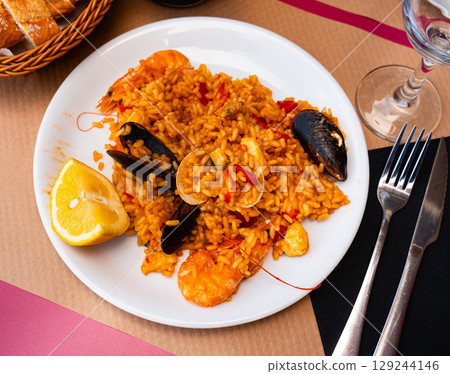 Paella made of rice and different seafood served in plate with table appointments 129244146