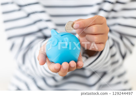Elementary school boy putting money into a blue piggy bank Elementary school boy putting money into a blue piggy bank 129244497