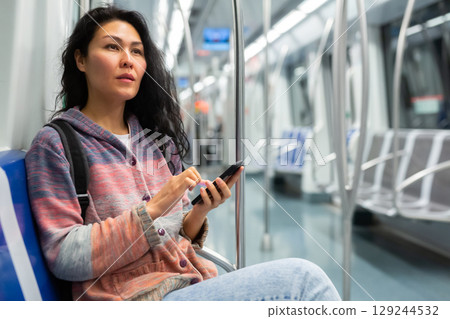 Woman passenger using phone in subway car Woman passenger using phone in subway car 129244532