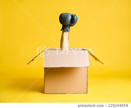 Hand in boxing glove raised up from open cardboard box 129244859