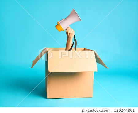 Hand with megaphone raised from cardboard box 129244861